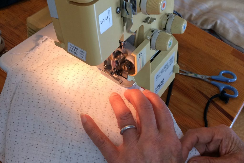 ロックミシンで麻の着物の裁断処理をする参加者